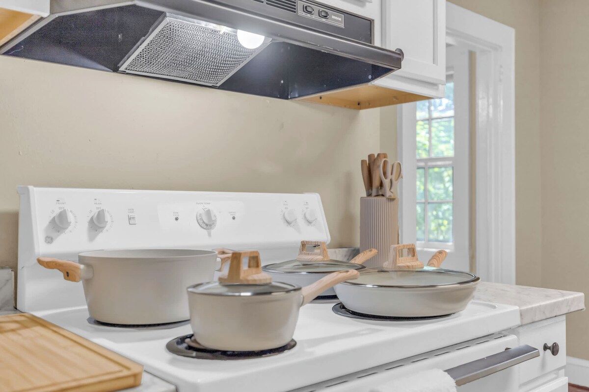 A kitchen with a white stove, pots, and a window with a view of greenery.