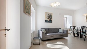 Un salon avec un canapé gris, une petite table et un coin repas avec des chaises.