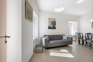 A living room with a grey sofa, a small table, and a dining area with chairs.