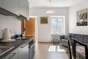 Una cucina moderna con un fornello, un lavello e un bollitore sul bancone. C'è un'area pranzo con un divano e un tavolo.