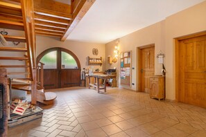 Un intérieur rustique avec un escalier en bois, un coin repas comprenant une table et des chaises, une grande porte en arc de cercle et des portes en bois.