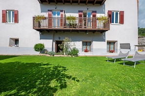 Un edificio a due piani con un balcone, un prato e due poltrone da relax.