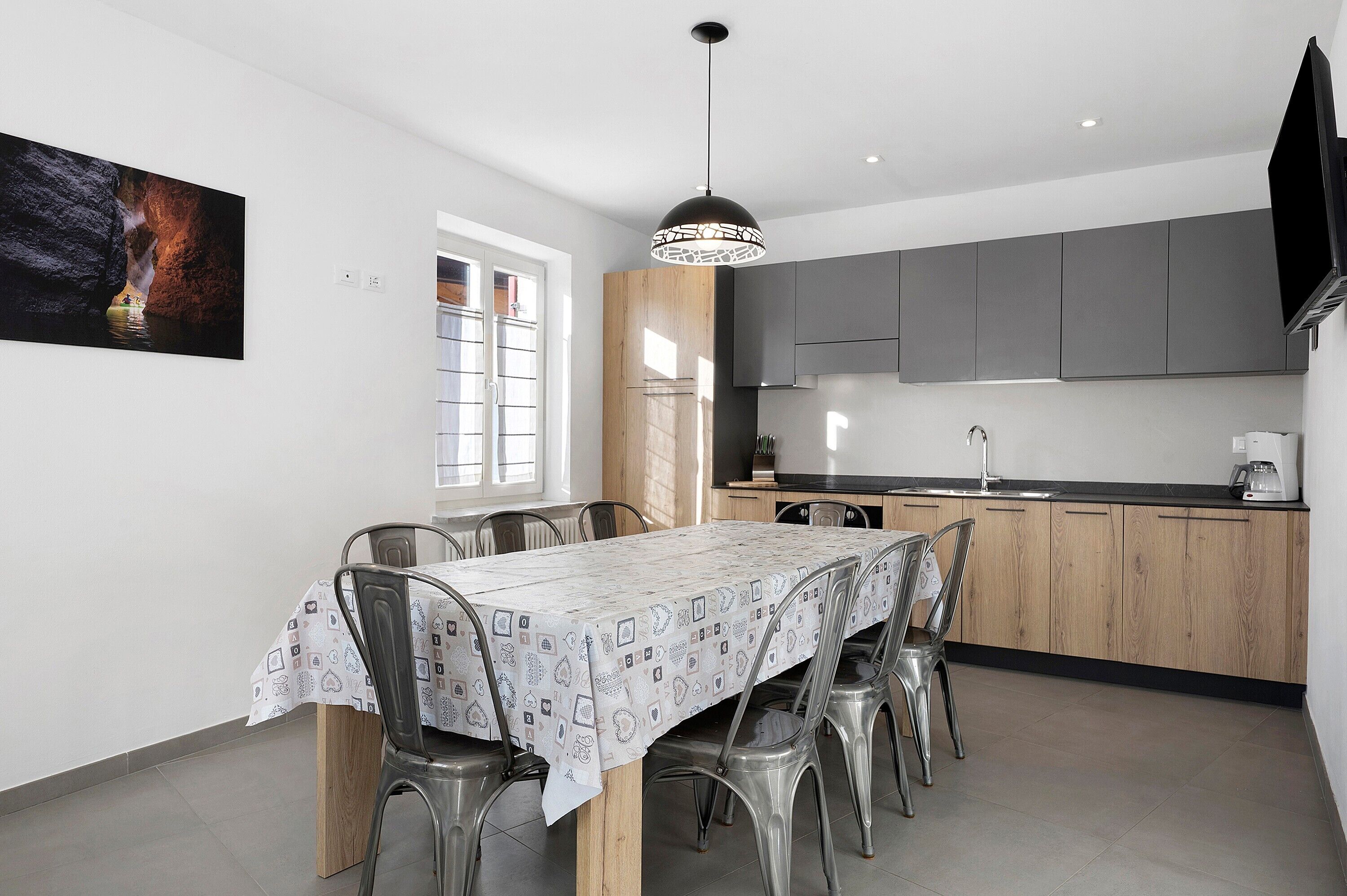 Une cuisine moderne avec des meubles de couleur grise, une table à manger avec des chaises et un luminaire suspendu.