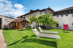 Eine Villa mit Steinmauer, Holzterrasse, Essbereich und Pool mit Liegestühlen.
