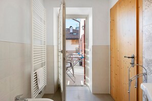 A bathroom with a white towel rack, a wooden door, and a view of a courtyard with a table and chairs.