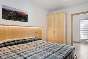A bedroom with a bed, wooden headboard, a wardrobe, a window with blinds, and a wall-mounted picture.
