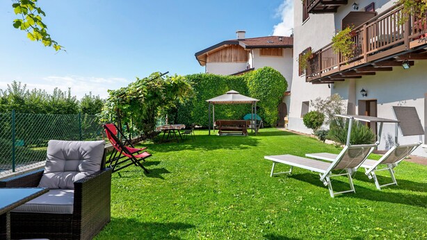 A well-maintained garden with outdoor furniture, a pergola, and a building with balconies. - Apartment 'La Canonica Pino' with Mountain View, Shared Garden and Wi-Fi (Brez)