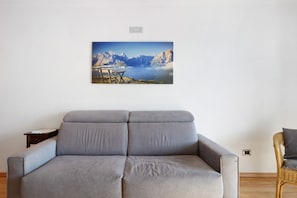 A modern living room with a grey sofa, a wicker chair, and a framed landscape painting on the wall.