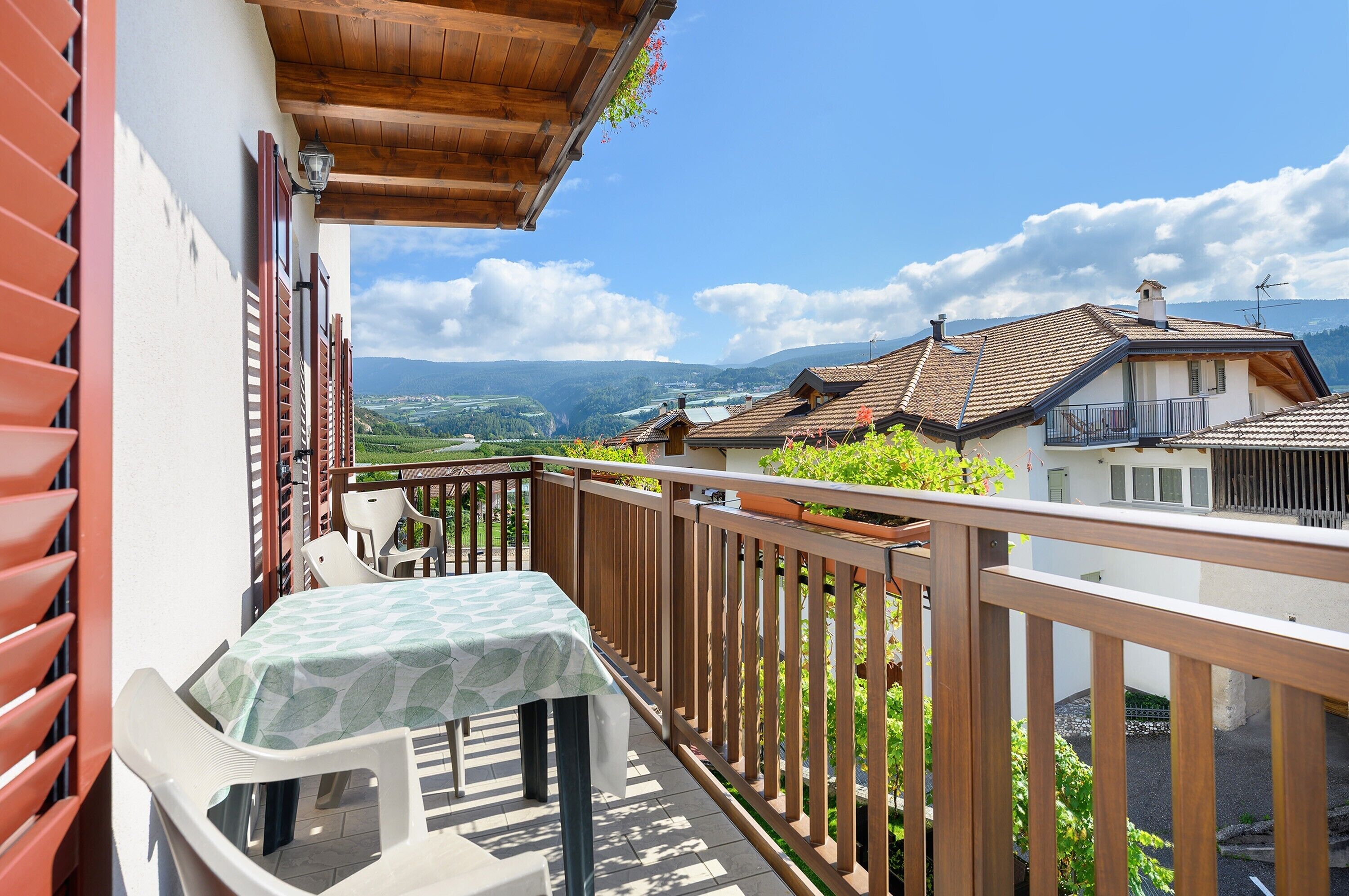 A balcony with a table and chairs, a wooden railing, and a view of a valley and mountains.