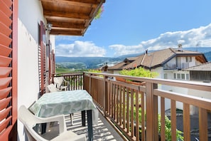 A balcony with a table and chairs, a wooden railing, and a view of a valley and mountains.