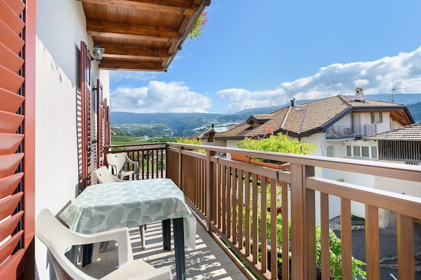 A balcony with a table and chairs, a wooden railing, and a view of a valley and mountains.