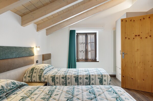 Et soveværelse med to senge, et vindue med gardiner, en trædør og et skråt loft.