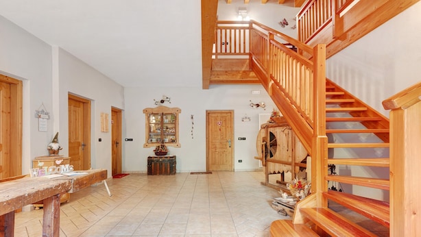 A spacious interior with a wooden staircase, a reception desk, and a tiled floor.