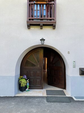 A building entrance with a large arched doorway, a small balcony above, and a mailbox on the wall.