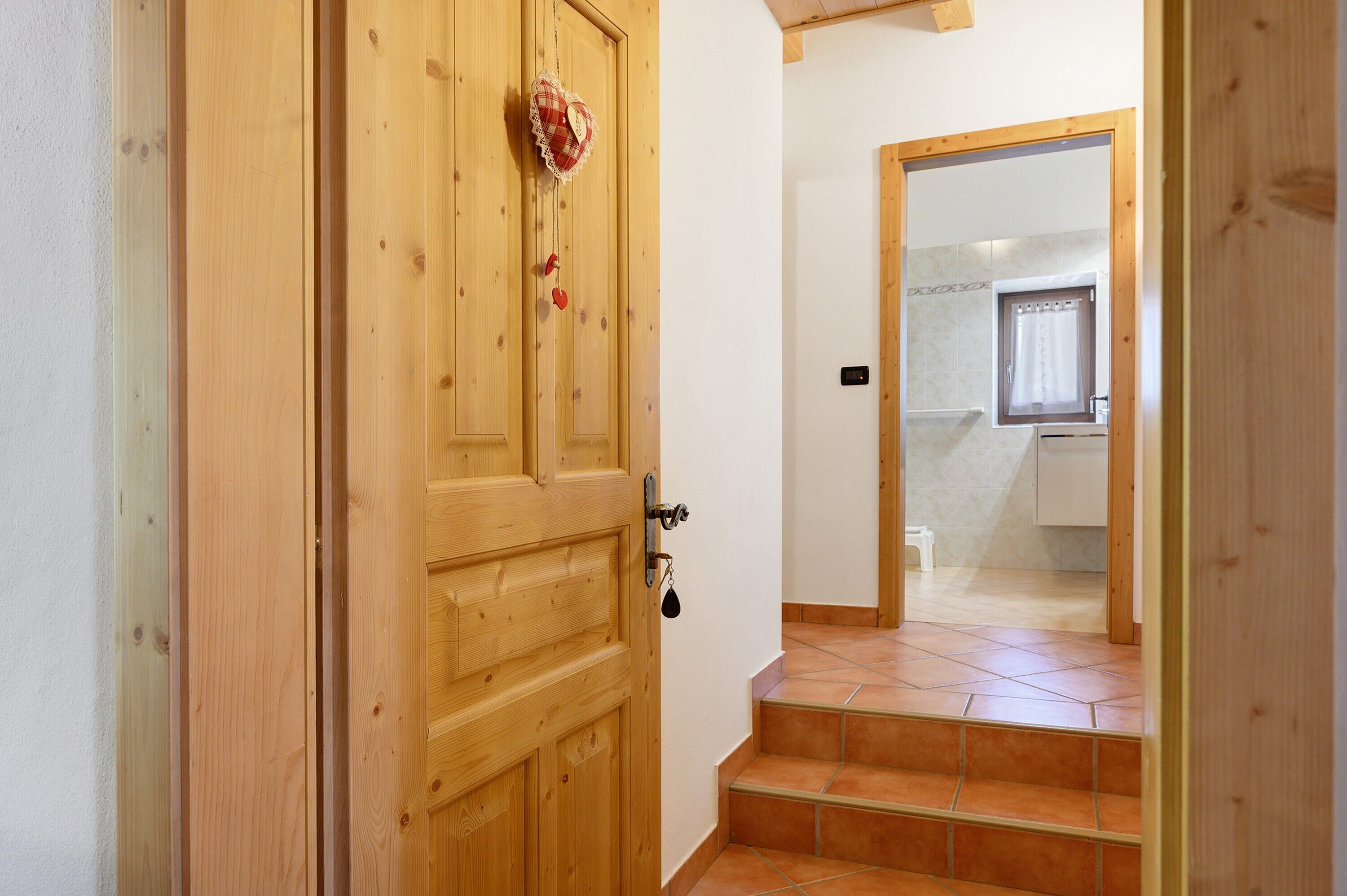 A wooden door with a heart-shaped decoration, a set of stairs leading to a bathroom with a shower and a window.