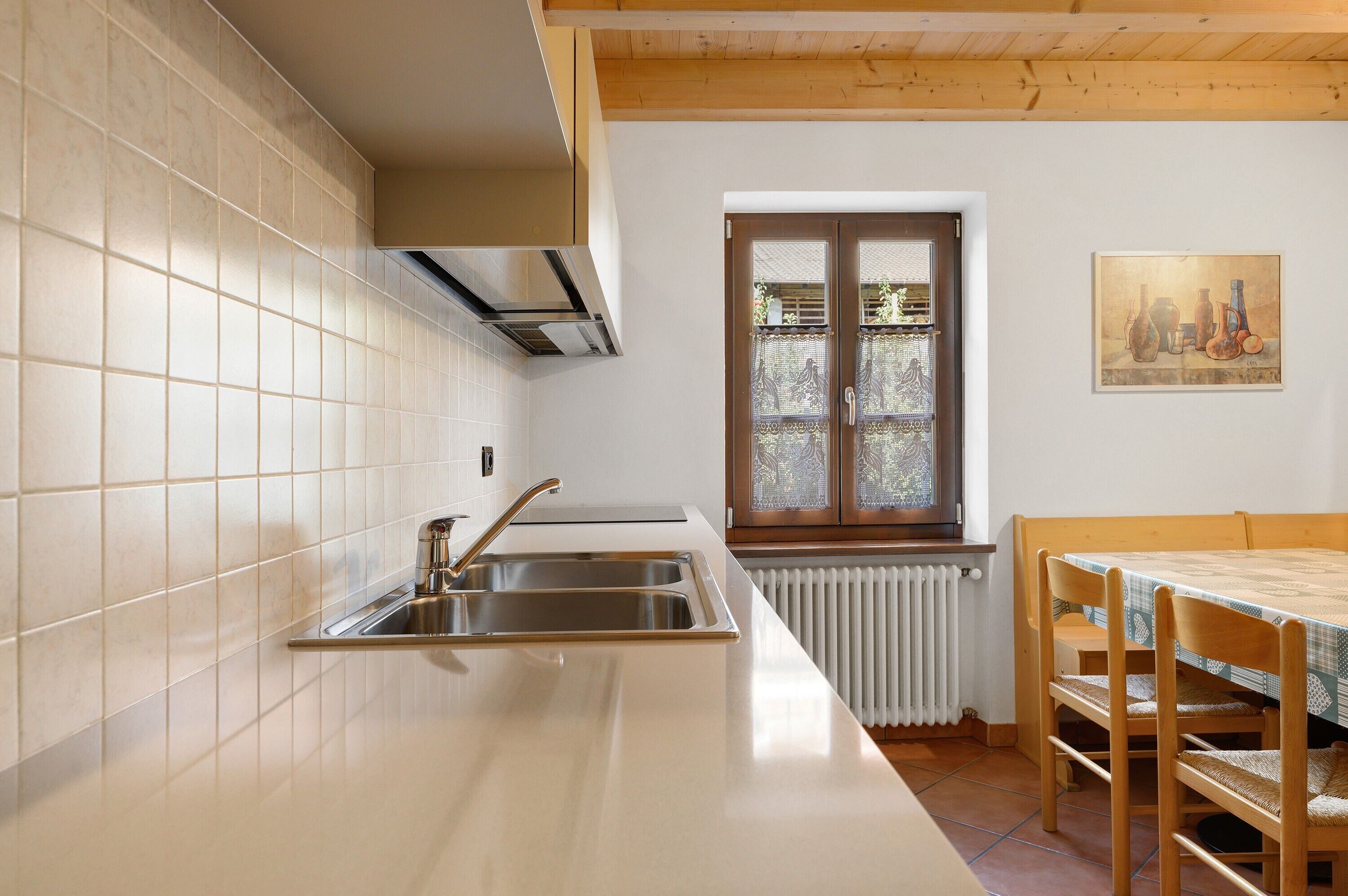 A kitchen with a stainless steel sink, a window with a view, and a dining table with chairs.