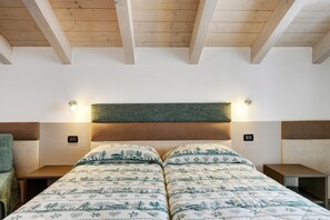 A bedroom with a wooden ceiling, a bed with patterned bedding, bedside tables, and wall-mounted lights.