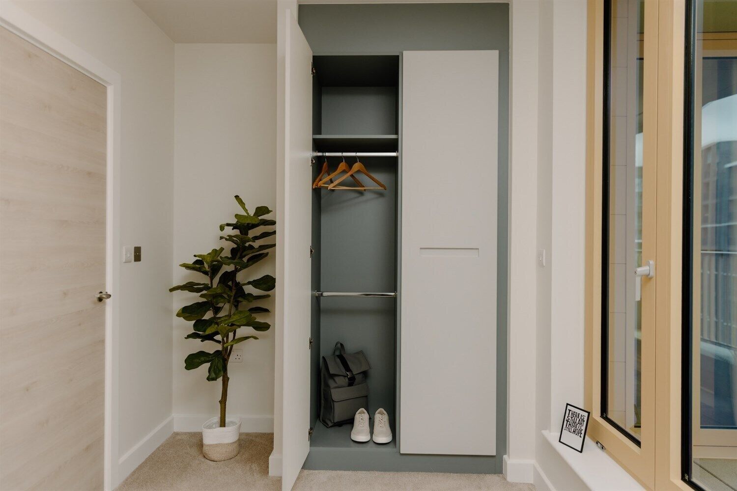 A walk-in closet with hanging space and a shoe rack, a potted plant, and a framed quote on the wall.