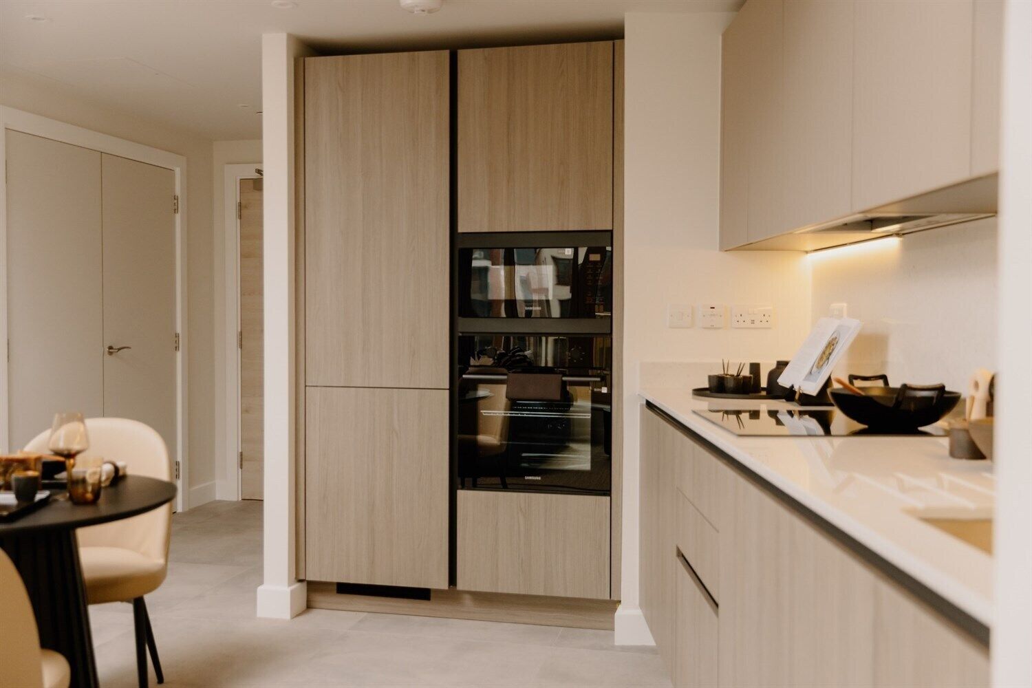 A modern kitchen with built-in appliances, a dining area with a table and chairs, and a separate dining room with a door.