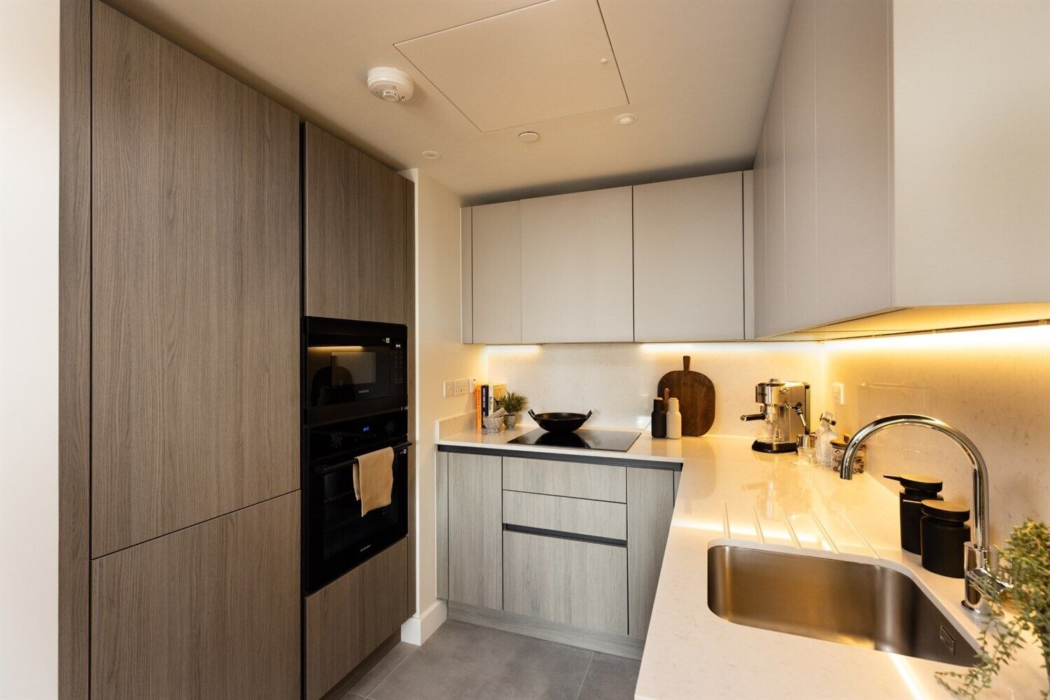 A modern kitchen with wooden cabinets, a black microwave, a sink, and a countertop with a kettle and a plant.