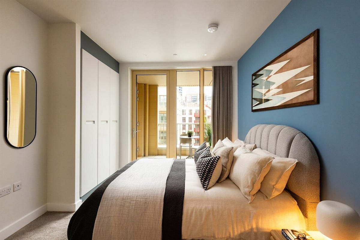 A modern bedroom with a large bed, a mirror, and a view of the city through the window.