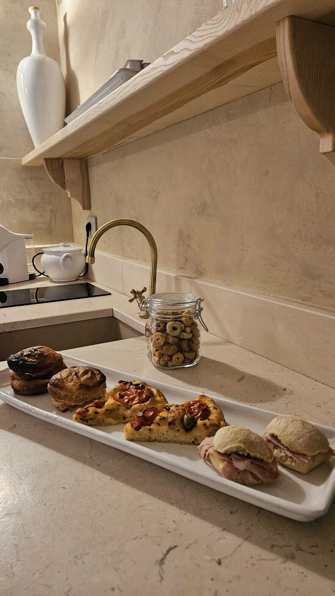 Una encimera de cocina con diversos alimentos, incluyendo pasteles, sándwiches y un tarro de aperitivos.