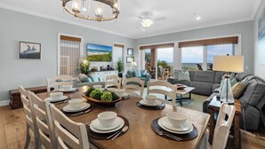 A dining area with a wooden table set for four, surrounded by white chairs. There is a chandelier above the table and a ceiling fan in the room. - Navarre Beachfront Townhome Southern Cross Sleeps 13 + Pet Friendly (Navarre)