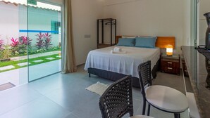 Une chambre à coucher comprenant un lit, une table de chevet, une lampe et une vue sur un jardin, visible à travers une porte vitrée.