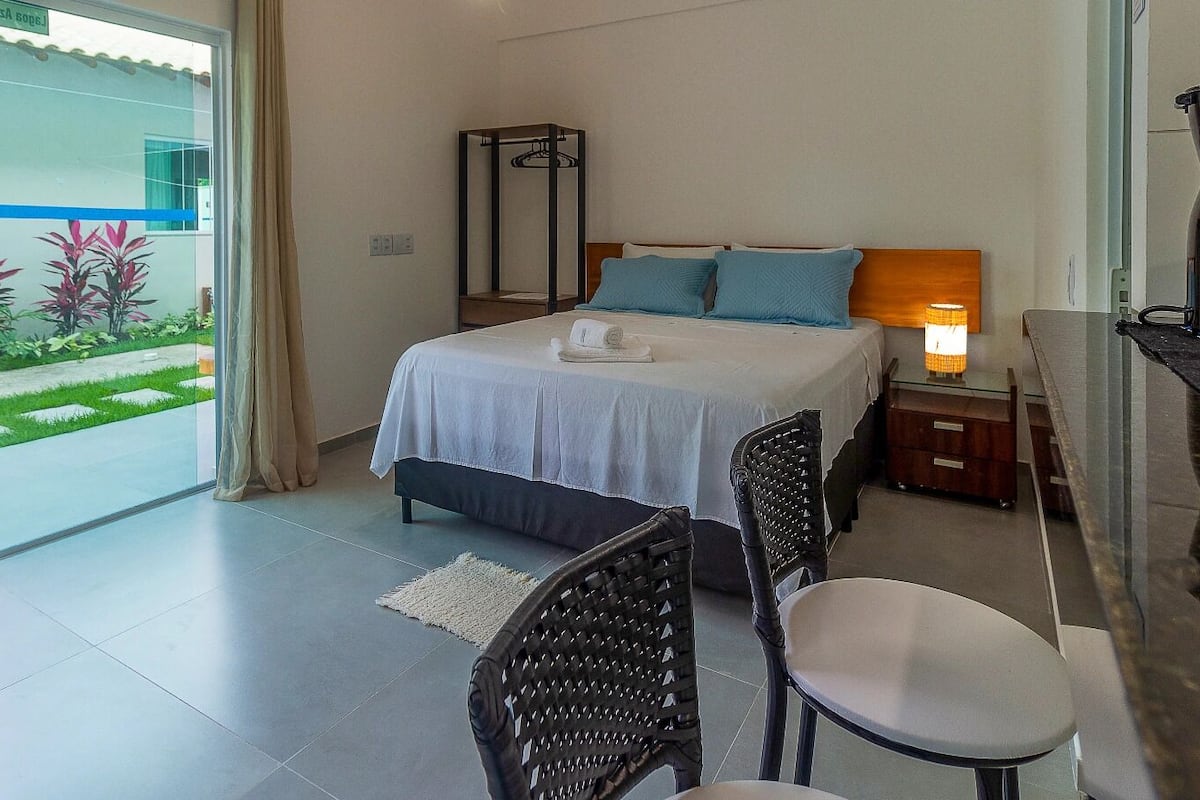 Una camera da letto con un letto, un comodino, una lampada e vista su un giardino attraverso una porta di vetro.