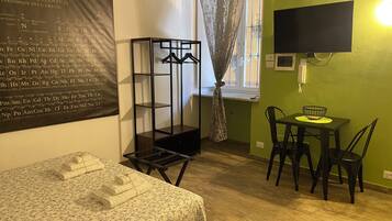 Ein Zimmer mit einem Bett, einem Tisch mit Stühlen, einem Fernseher und einem Wandregal.