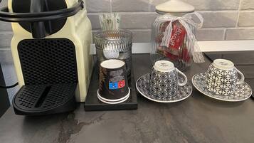 A kitchen counter with a coffee maker, a glass container with a tea bag, and a jar of biscotti.