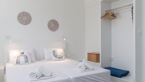 Une chambre d’hôtel avec un lit soigneusement fait, deux éléments décoratifs accrochés au mur, une armoire en bois et une serviette bleue posée sur le sol.