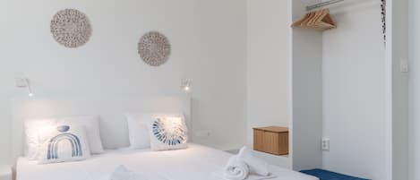 A hotel room with a neatly made bed, two decorative wall pieces, a wooden cabinet, and a blue towel on the floor.