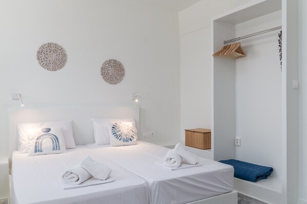 A hotel room with a neatly made bed, two decorative wall pieces, a wooden cabinet, and a blue towel on the floor.