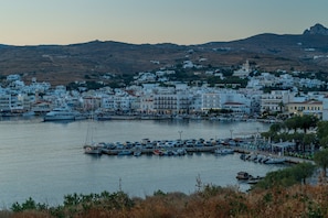Un pueblo costero con edificios blancos, un puerto deportivo con barcos y un paisaje montañoso de fondo.
