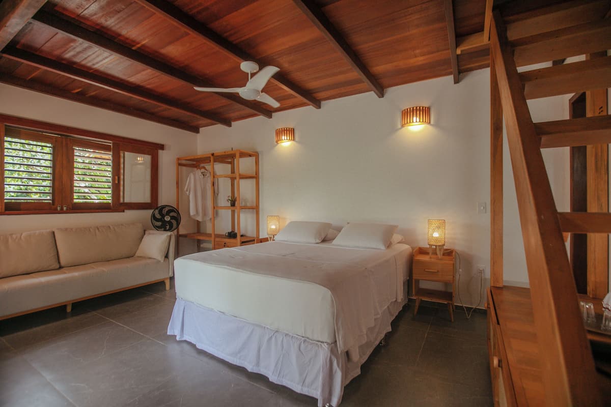Une chambre à coucher avec un lit, un plafond en bois, une chaise en bois, une table de chevet et une fenêtre avec des stores.