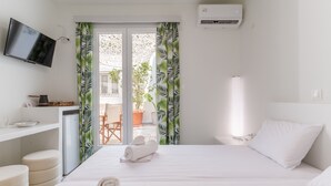Ein Hotelzimmer mit Bett, Fernseher, Schreibtisch, Stuhl und einem Balkon mit Vorhängen.