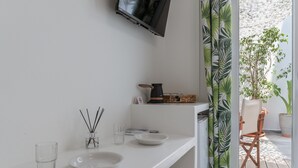 Ein sauberes, modernes Zimmer mit einer weißen Arbeitsplatte, einem an der Wand befestigten Fernseher und Blick ins Freie durch ein Fenster mit Vorhang.
