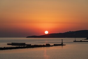 A sunset over a calm body of water with a distant hill and a lighthouse.