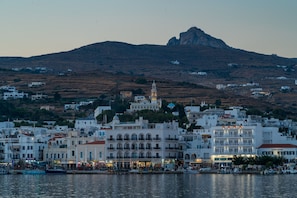 A coastal town with white buildings, a prominent church with a bell tower, and a hill in the background.