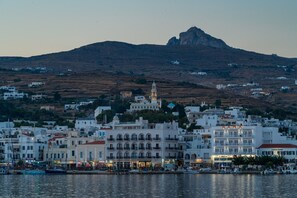 A coastal town with white buildings, a prominent church with a bell tower, and a hill in the background.
