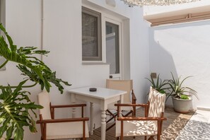 A white exterior wall, a window, a door, a white table, and two wooden chairs. - (Τήνος)