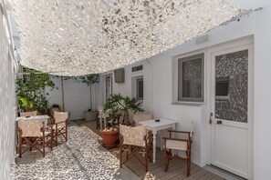 A covered outdoor seating area with tables and chairs, potted plants, and a white door. - (Τήνος)