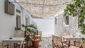 Un espacio al aire libre con patio, muebles de madera, plantas en macetas y una pared blanca.