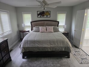 Un dormitorio con cama, mesitas de noche, ventilador de techo, puerta y ventana con persianas.