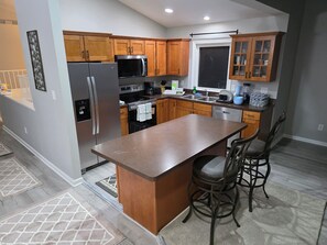 Una cocina moderna con armarios de madera, electrodomésticos de acero inoxidable, una isla central con taburetes altos y una ventana sobre el fregadero.