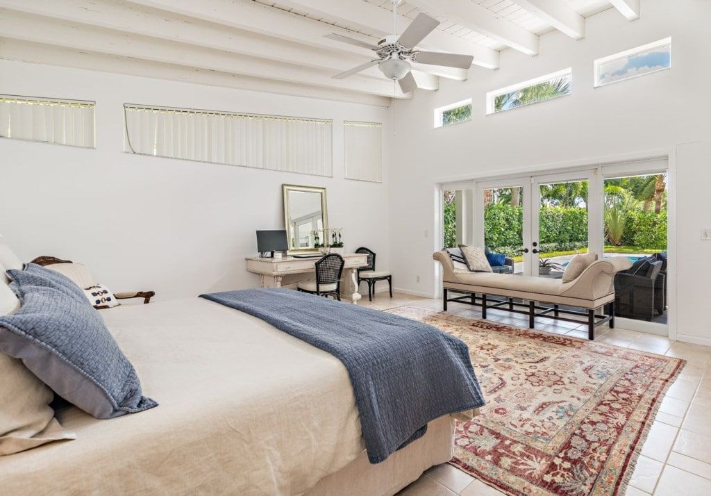 A bedroom with a bed, a desk, a chair, a sofa, a large window, and a ceiling fan.