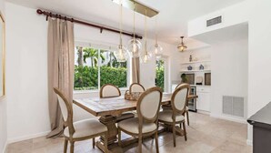 Un comedor con una mesa y sillas de madera, una lámpara colgante y vistas a zonas verdes al exterior.