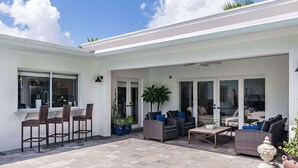 Una casa moderna con patio amoblado con muebles de mimbre, plantas en macetas y una vista despejada del cielo.