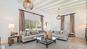 Amplia sala de estar con una mesa de centro de vidrio, sofá color beige y dos lámparas.